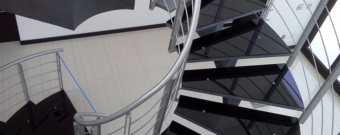 Escalera helicoidal con escalones de cristal negro y barandal metálico